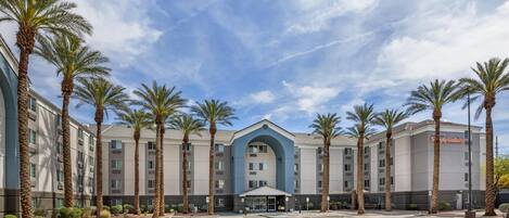A hotel with a central entrance, multiple floors, and palm trees.