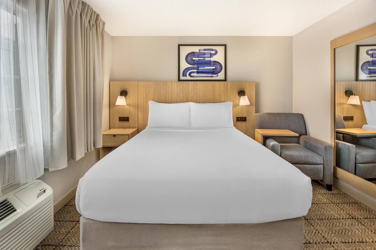 Hotelkamer met een groot bed, twee nachtkastjes met lampen, een stoel, een spiegel en een wanddecoratie.