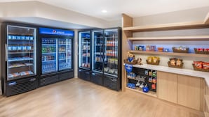 Un interior limpio y moderno con tres dispensadores refrigerados para bebidas, una zona que admite mascotas con golosinas para perros y una variedad de aperitivos en estantes.