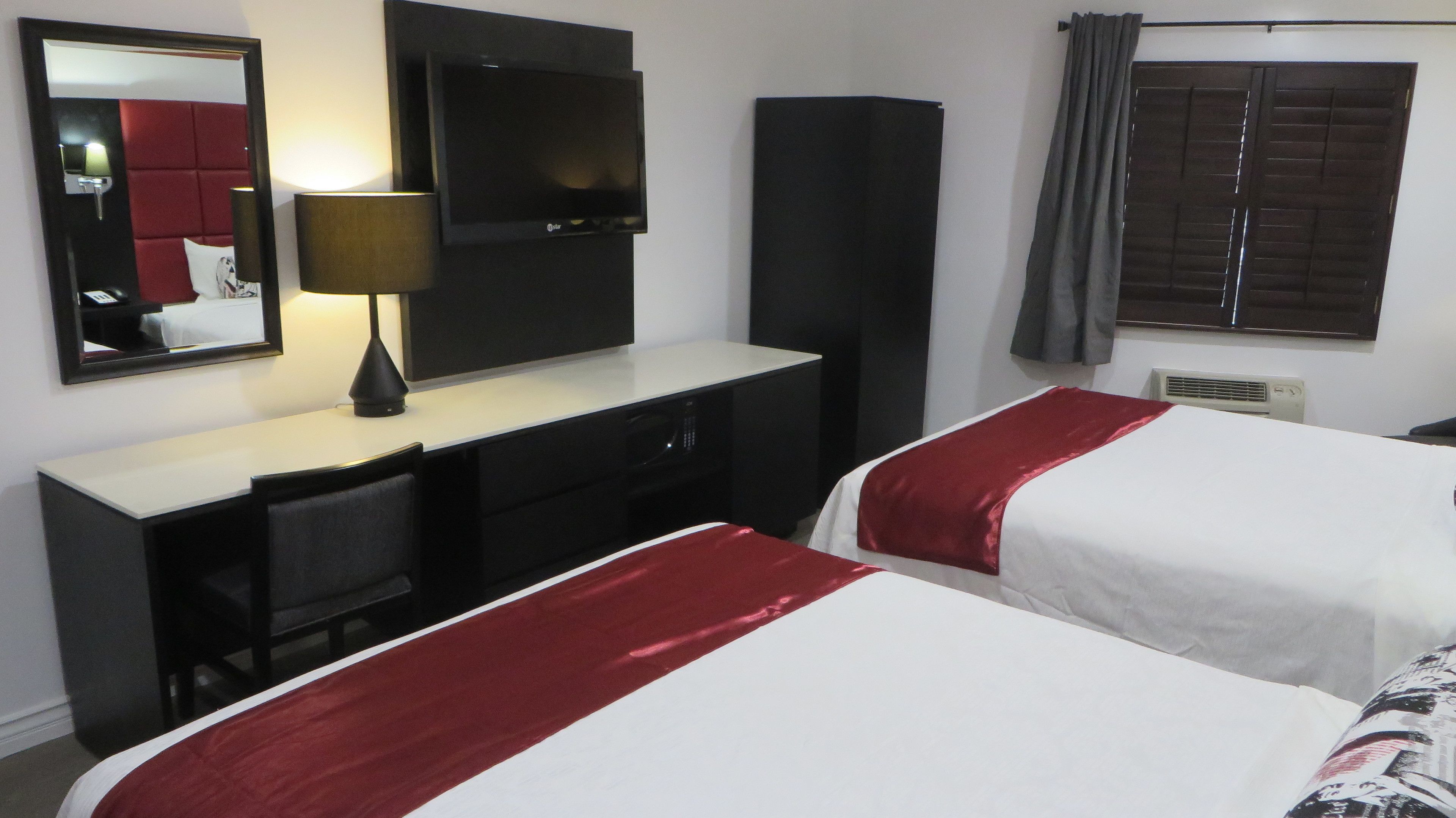 Habitación de hotel con dos camas, un escritorio, un televisor, un espejo y una ventana con cortinas.