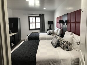 A hotel room with two beds, a desk, a wardrobe, a window with curtains, and a television. - Legend Hotel Hollywood (Los Angeles)