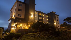 A multi-story building with a prominent central tower, multiple windows, and a well-lit entrance area.