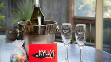 A bottle of champagne in a metal bucket, two glasses, a red card with "KYLLO'S seafood grill" logo, and a small bag of chocolates on a wooden table.