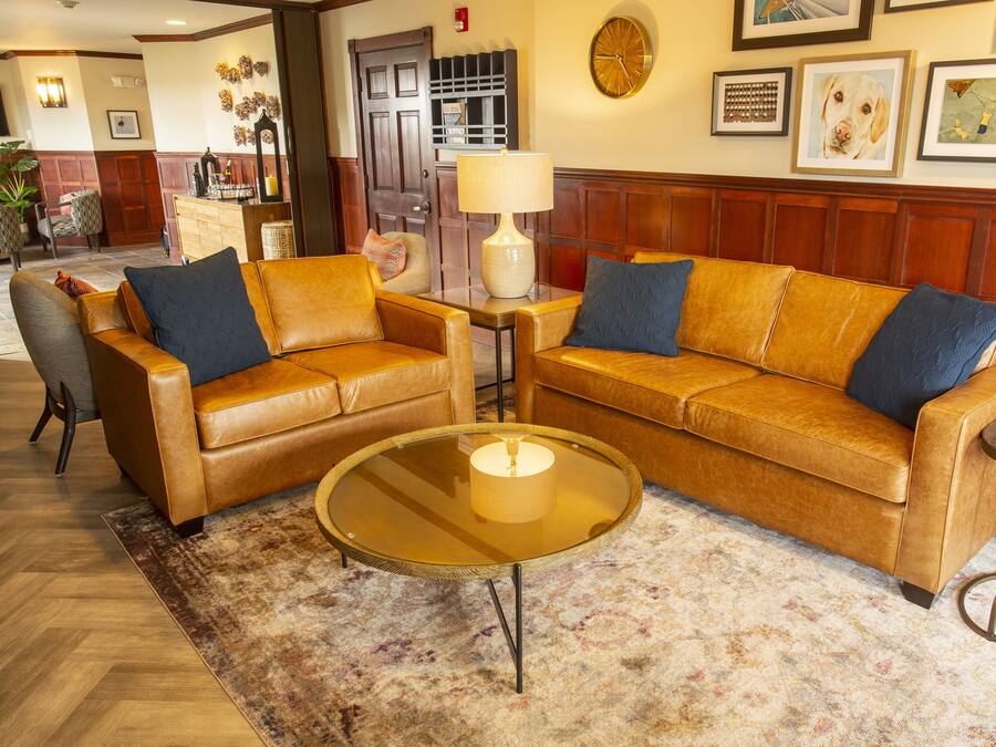 A lobby with a brown leather sofa, a glass coffee table, and a patterned rug.