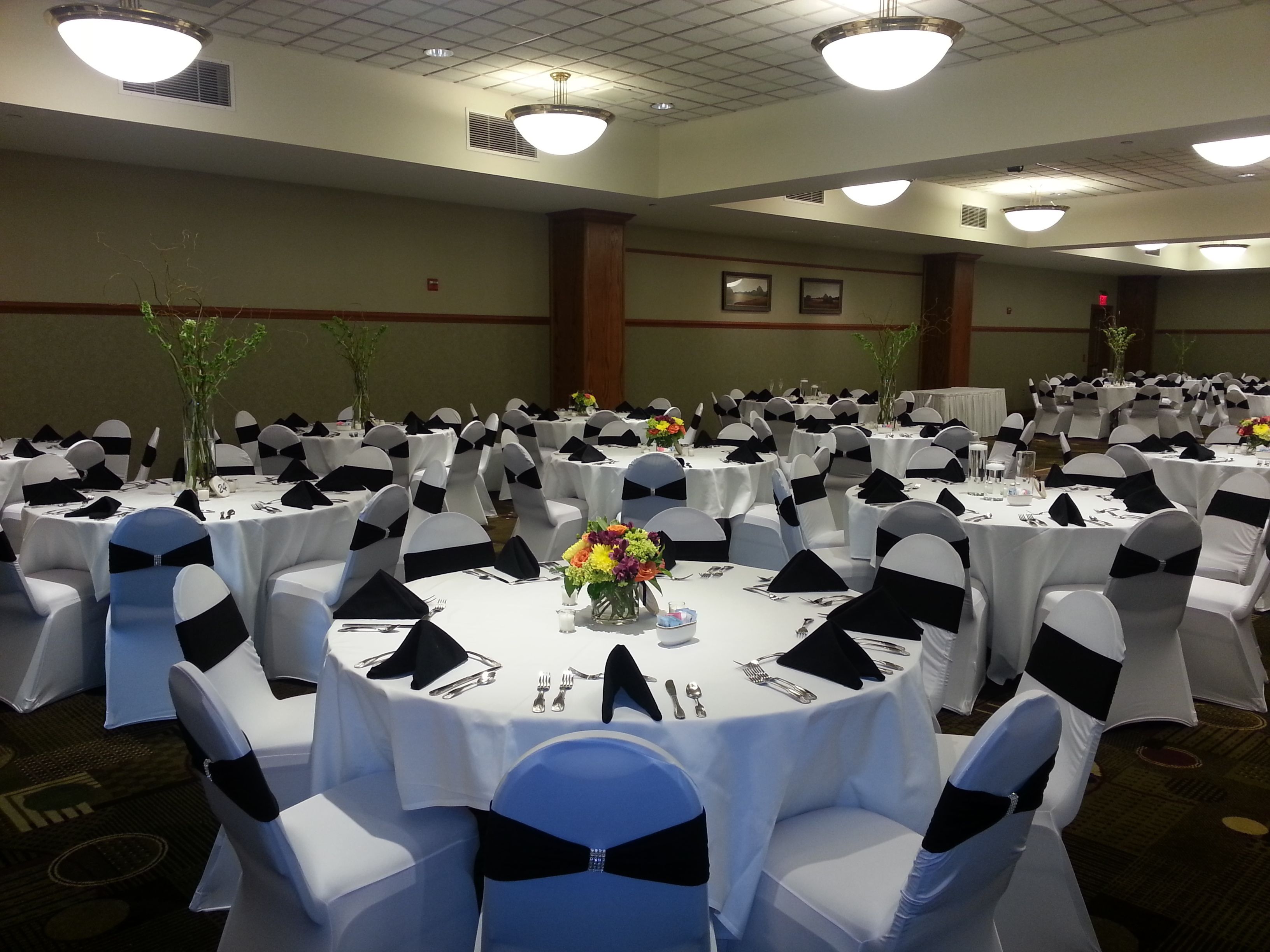 Un salón de banquetes con mesas redondas, manteles blancos y sillas con cintas negras.