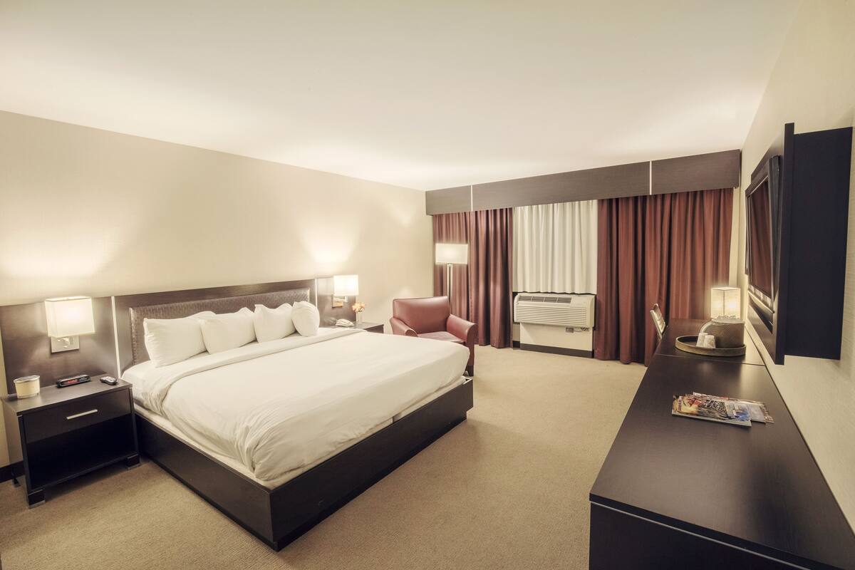 A hotel room with a large bed, a desk, a chair, and a TV.