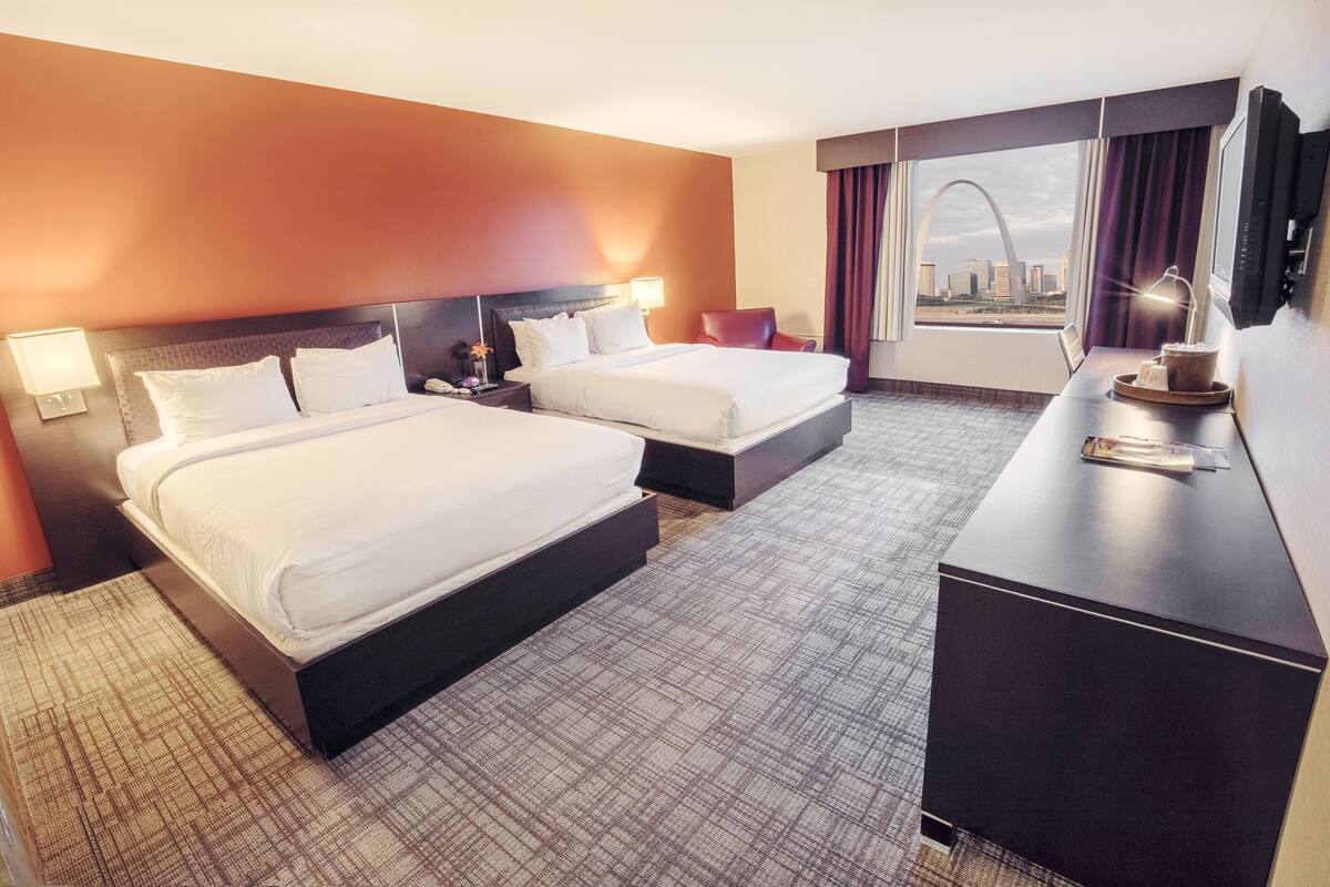 A hotel room with two beds, a desk, and a view of the cityscape.