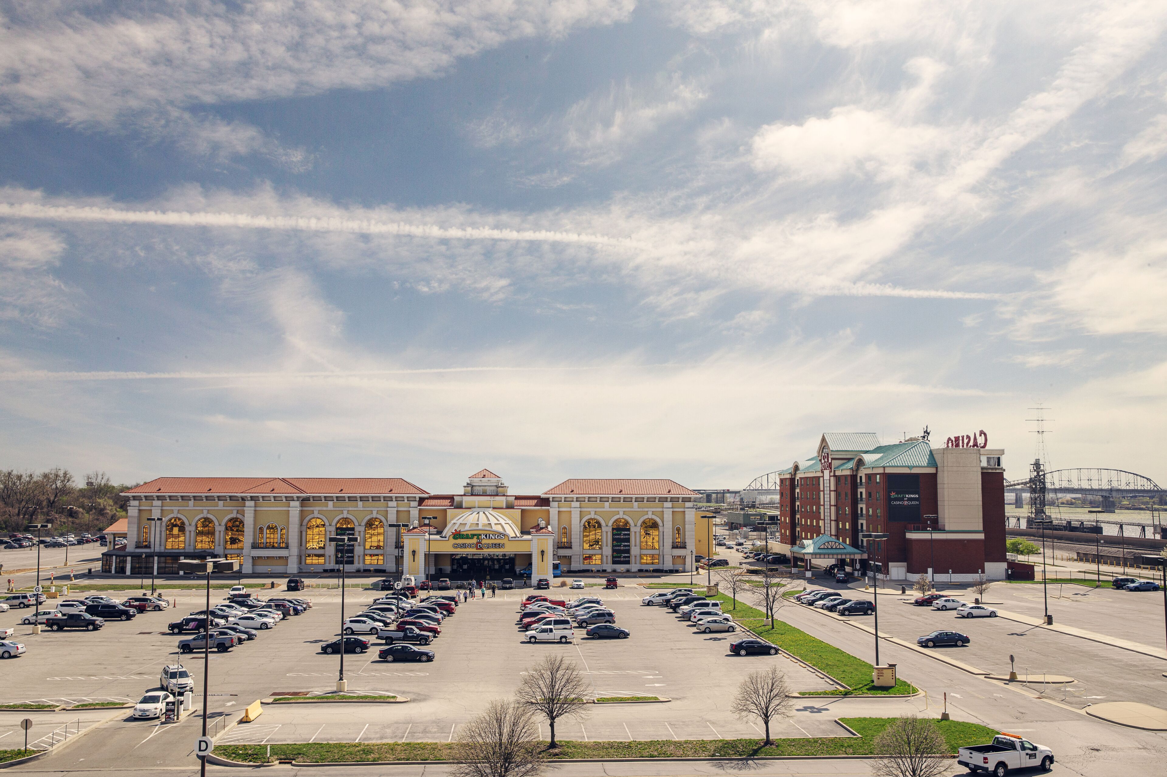 A large building with a central dome and arched windows, surrounded by a parking lot and a bridge in the background.