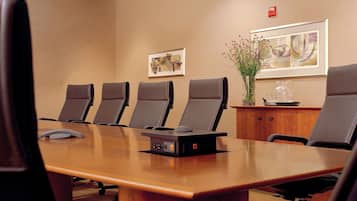 Uma sala de conferências com uma mesa comprida, seis cadeiras pretas, um púlpito e um vaso de flores ao lado.