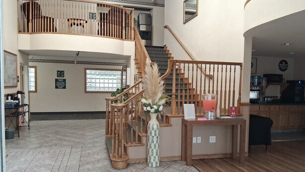 Um hall amplo com escadaria de madeira, balcão de recepção e vista para o andar superior.