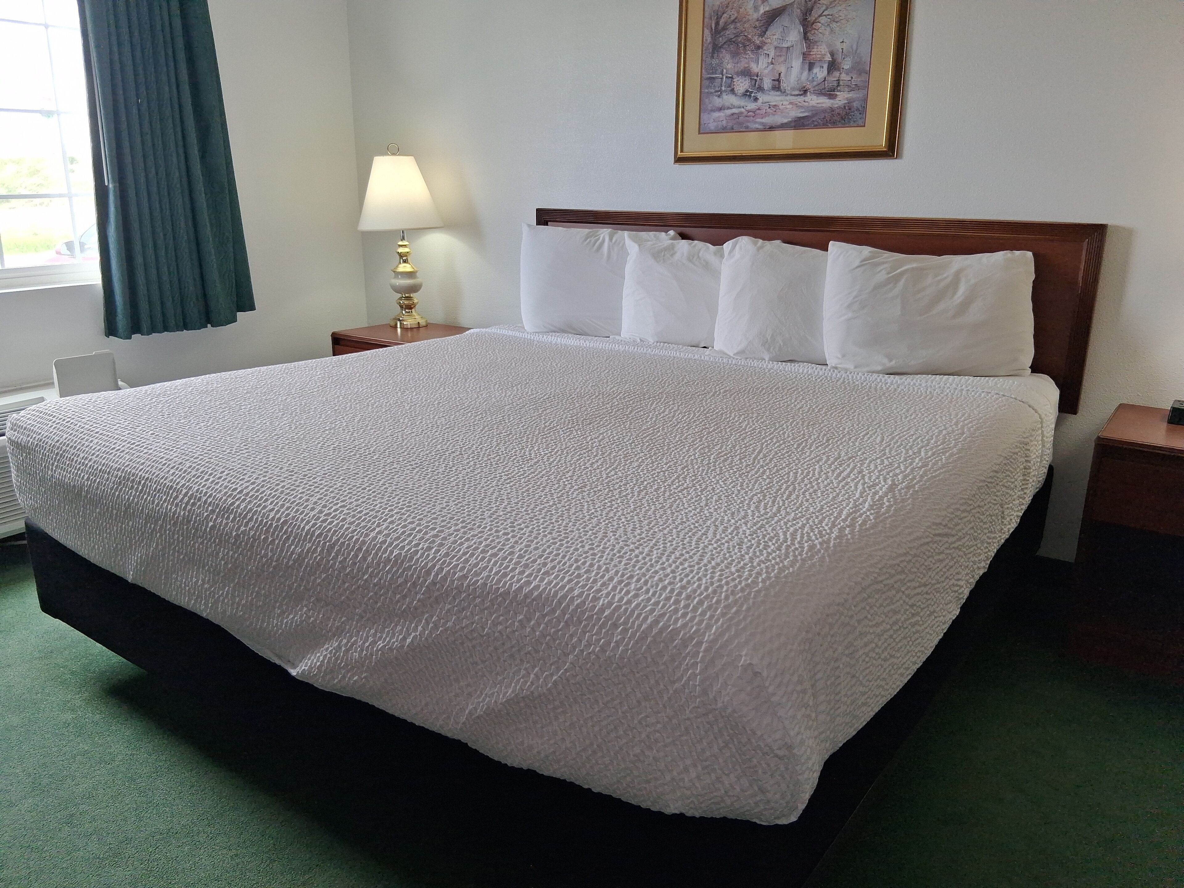 Una cama bien hecha con ropa blanca, un cabecero de madera y una lámpara de noche.