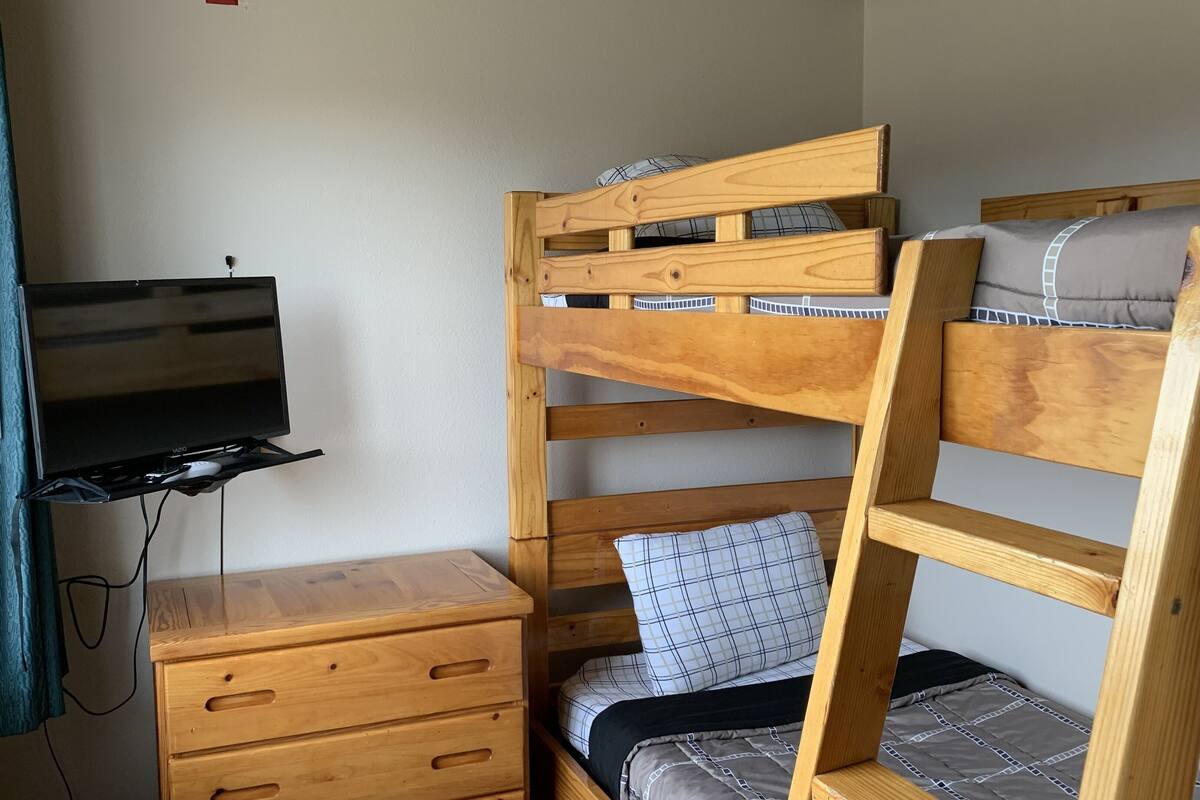 A bunk bed with a TV mounted on a wooden dresser below.