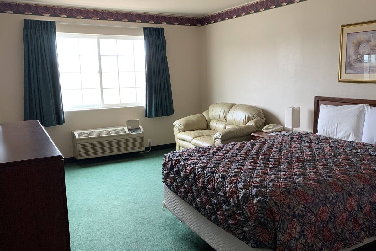 A hotel room with a bed, a chair, a desk, and a window with curtains.