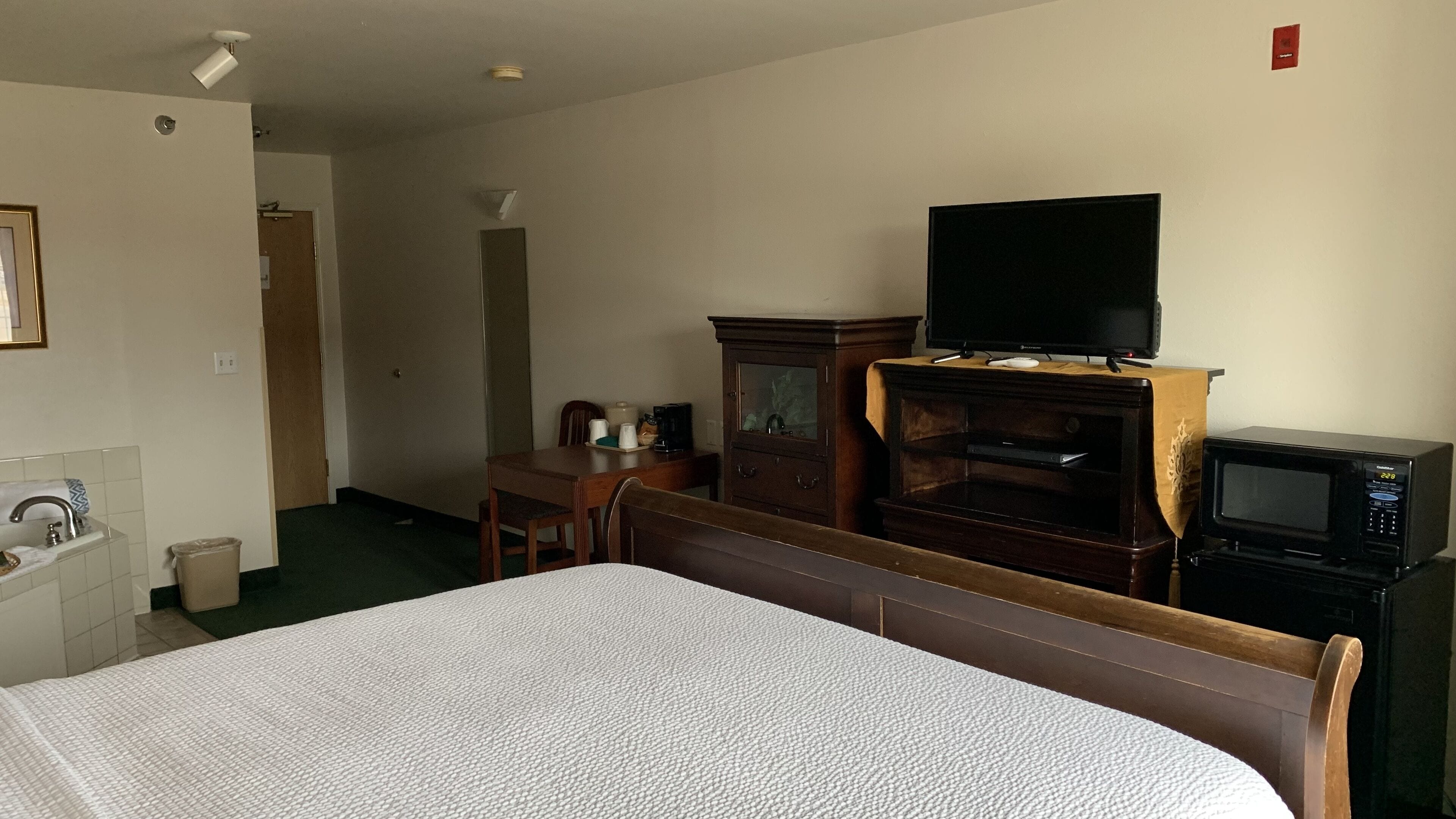A hotel room with a bed, a television, a microwave, a wooden cabinet, a desk, and a chair.