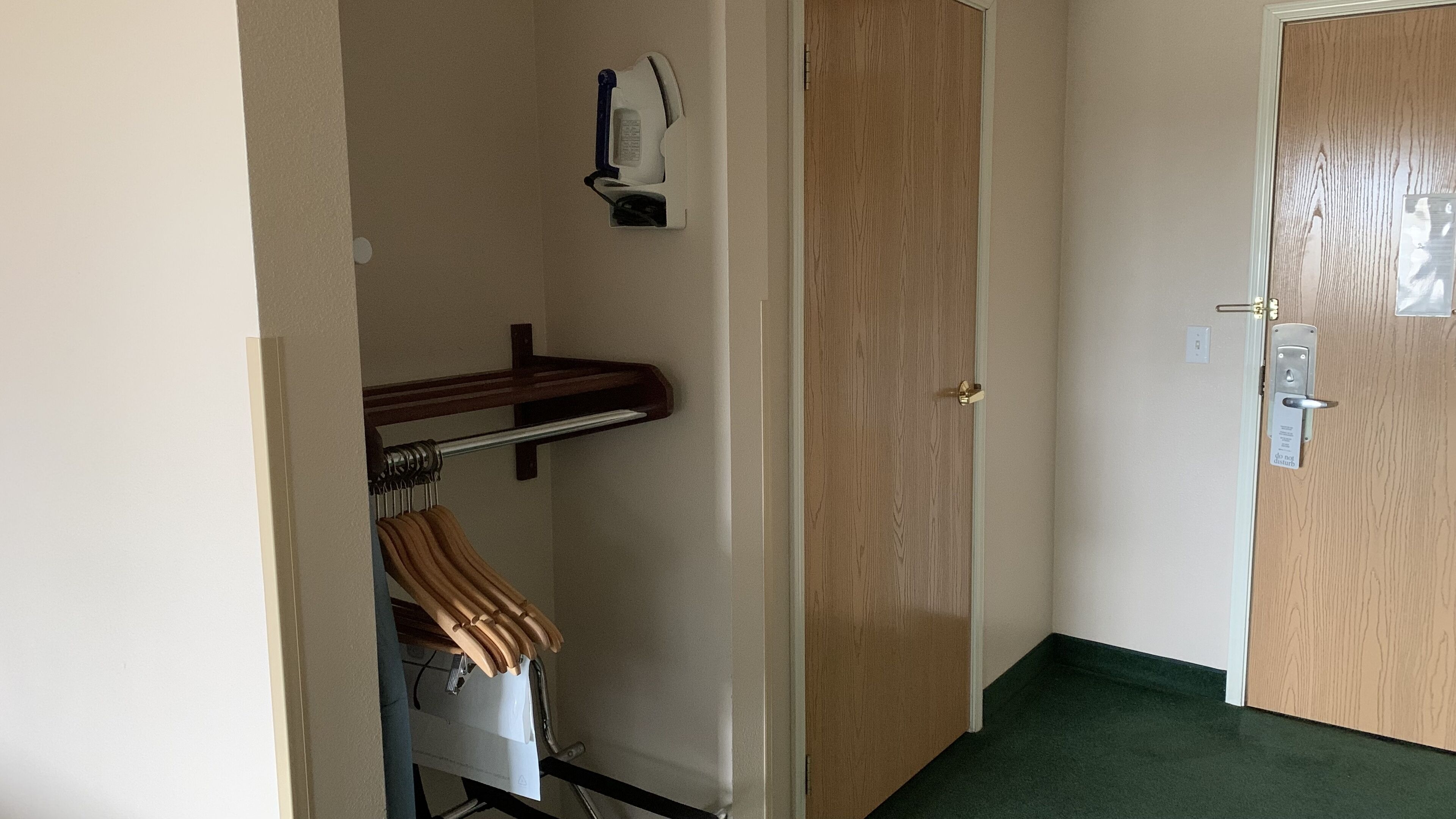 Una habitación con una puerta de madera, un perchero con una toalla a rayas, un estante con un objeto blanco y una alfombra verde.