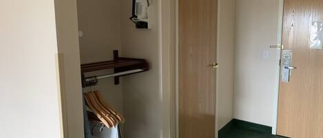 Een kamer met een houten deur, een kapstok met een gestreepte handdoek, een klein plankje met een wit voorwerp, en een groen tapijt.
