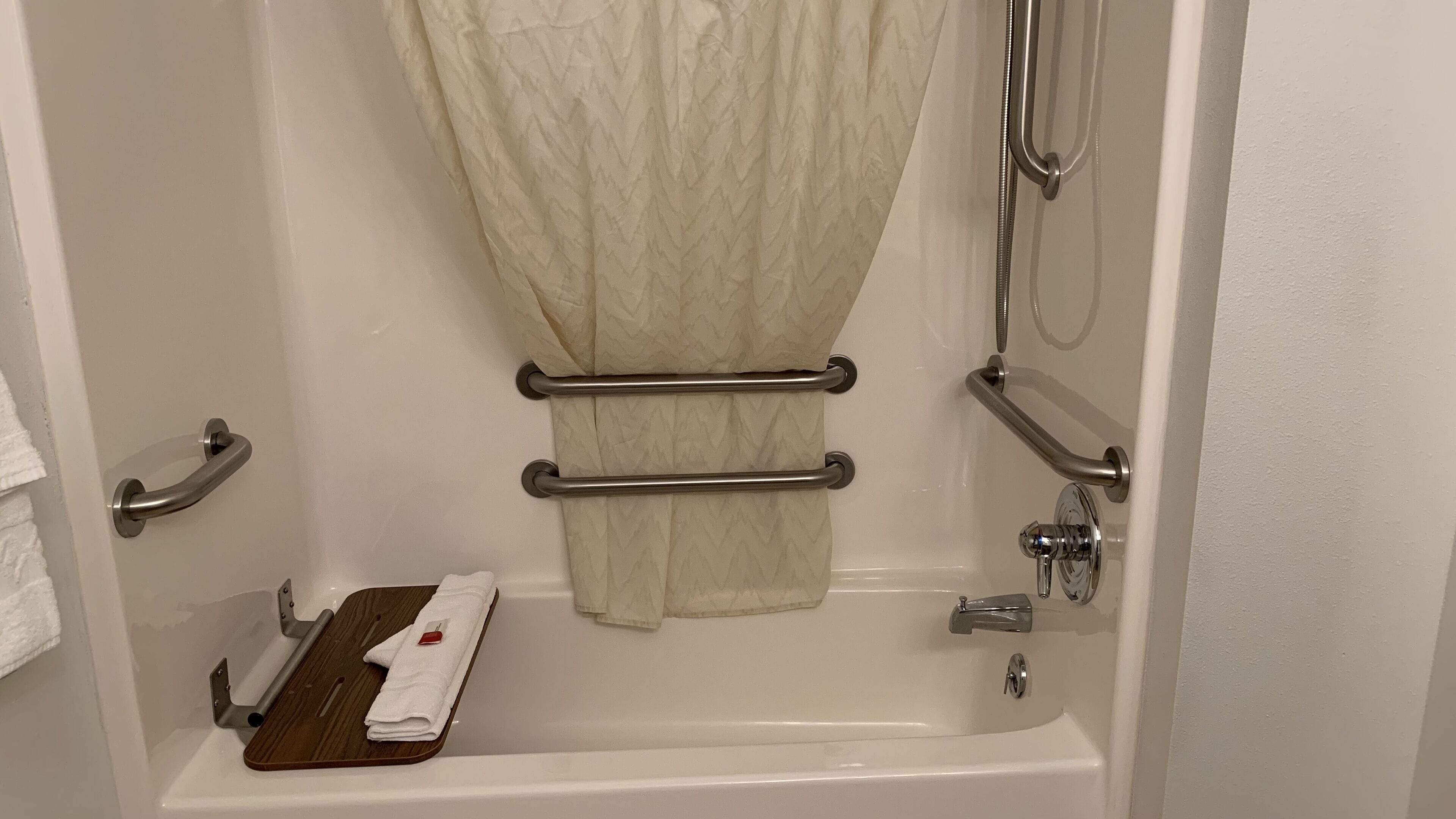 A bathroom with a bathtub, grab bars, a towel rack, and a wooden tray.