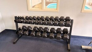 Uma barra com halteres em um quarto com carpete azul e quadros nas paredes.