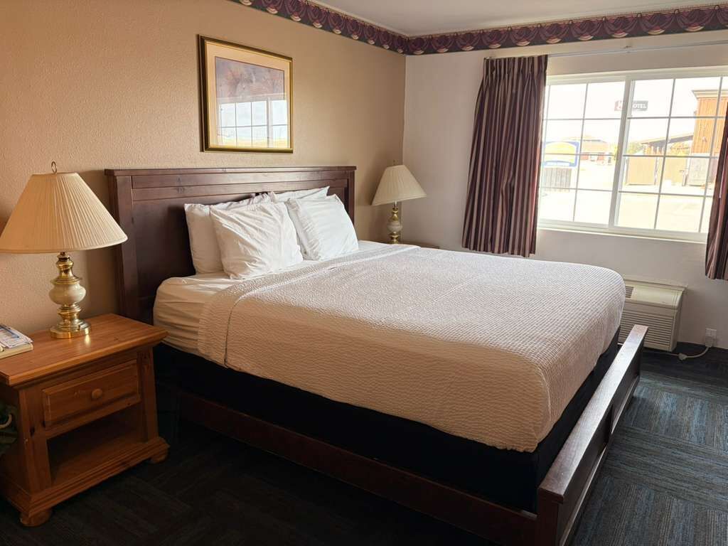 A hotel room with a large bed, two bedside lamps, a framed picture on the wall, and a window with curtains.