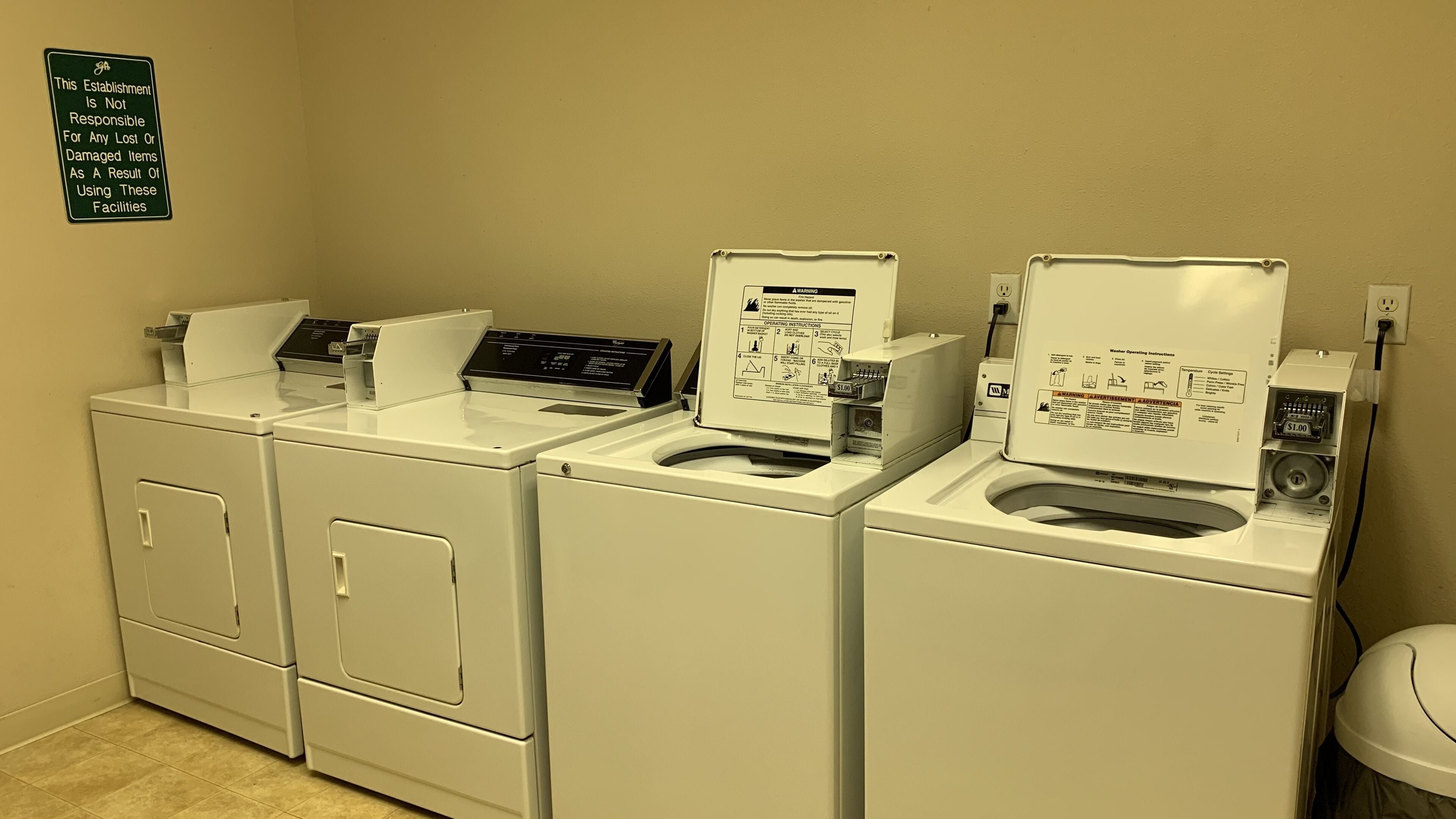 A laundry area with three washers and dryers, a sign indicating the establishment is not responsible for lost or damaged items, and a coin-operated dryer with a $1.00 fee.