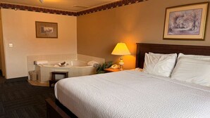 Quarto de hotel com uma cama grande, uma banheira, um abajur e um quadro na parede.