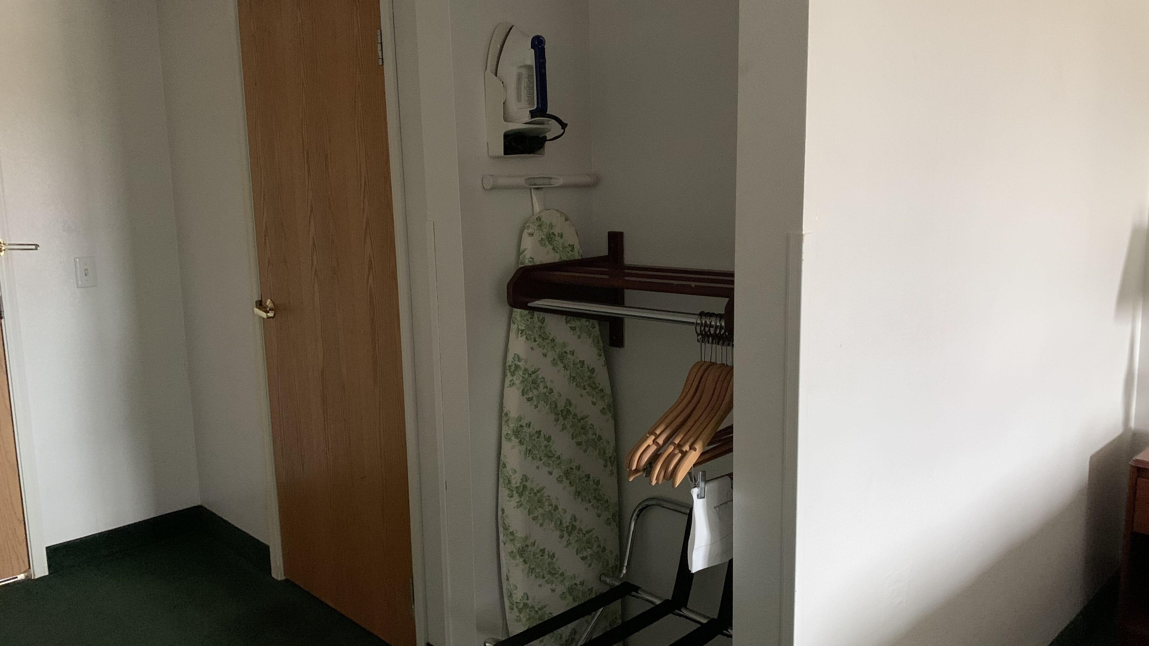 Un couloir avec une porte en bois, un mur blanc et un étendoir à linge sur lequel est suspendu un vêtement à motifs floraux.