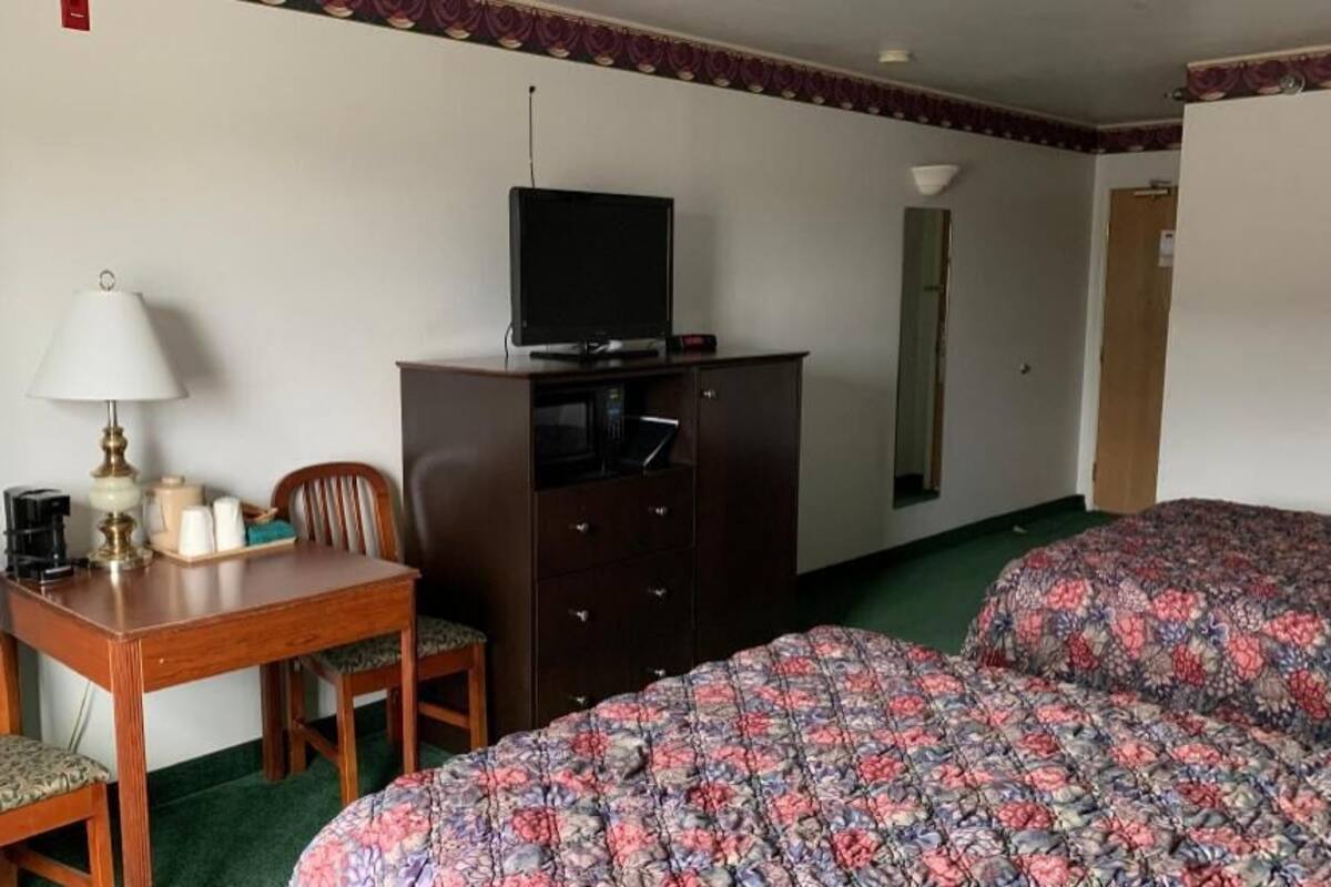 A hotel room with a bed, a desk with a lamp, a television on a cabinet, and a mirror on the wall.