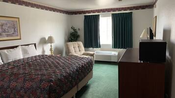 A hotel room with a large bed, a chair, a desk with a TV, an air conditioner, and a window with curtains.
