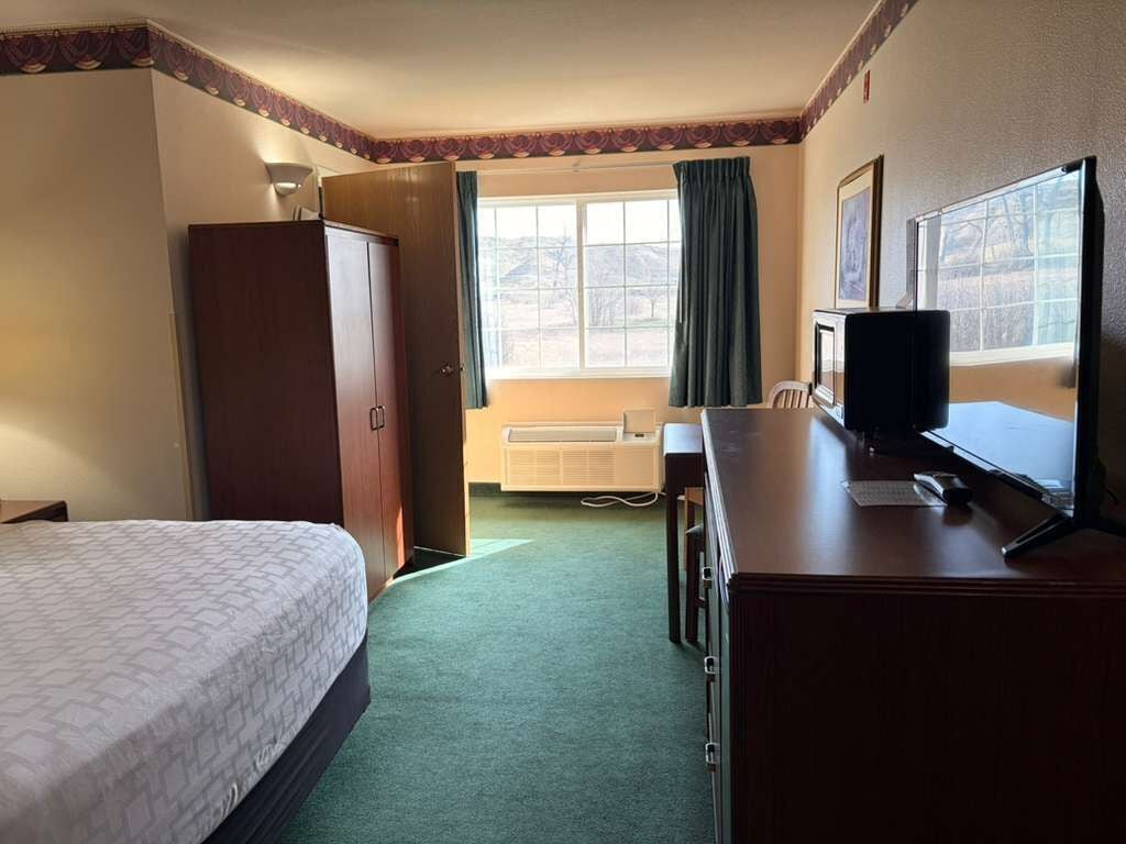 A hotel room with a bed, a desk with a computer, a wardrobe, and a window with curtains.