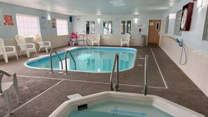 Piscina interior com duas áreas distintas, placas de segurança e cadeiras brancas ao redor da área da piscina.