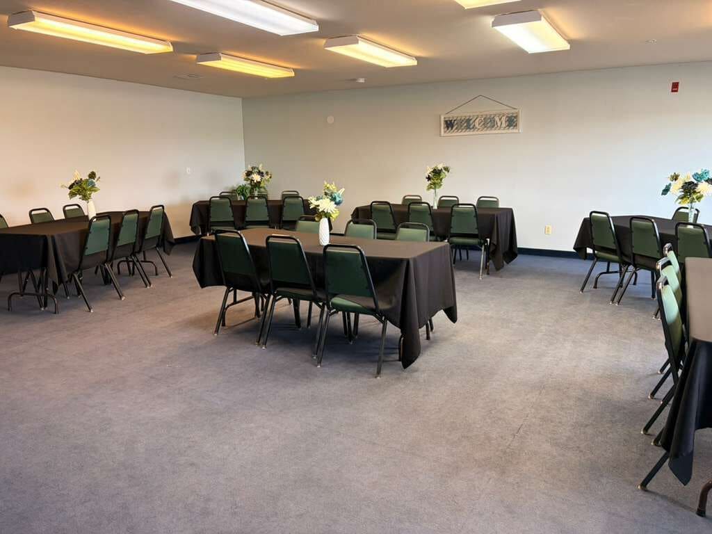 A conference room with tables and chairs, carpeted floor, and ceiling lights.