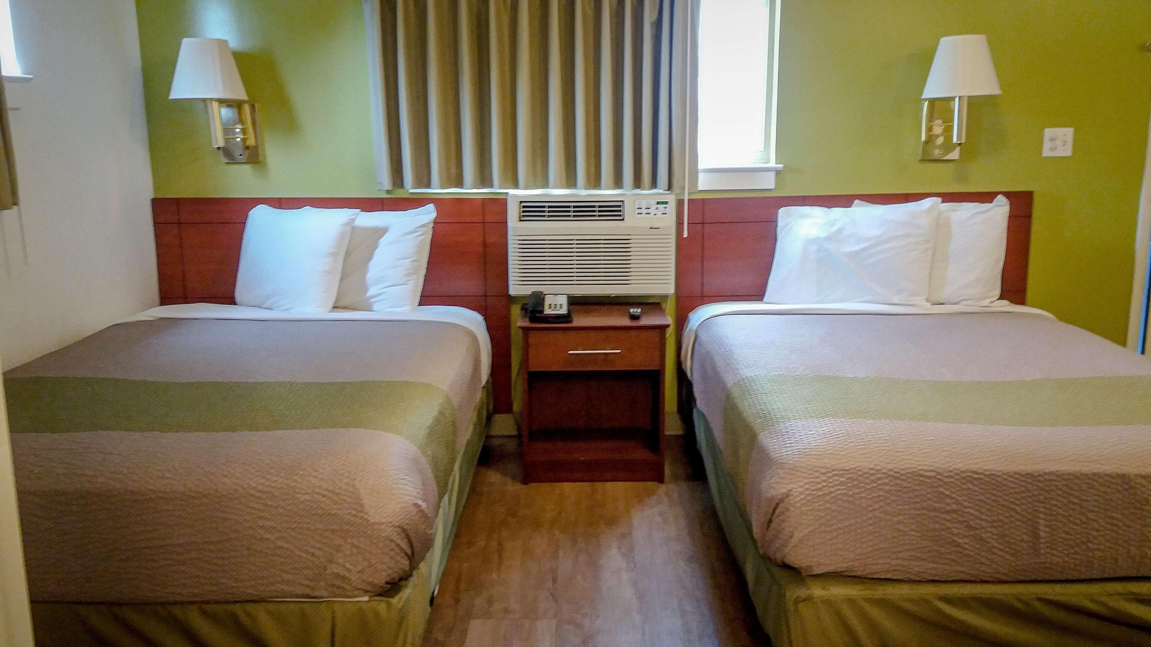 Habitación de hotel con dos camas, una mesita de noche, una lámpara y un equipo de aire acondicionado.