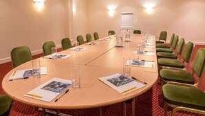 Ein Konferenzraum mit einem langen Tisch, grünen Stühlen und einer Tafel.