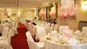 Ein Festsaal mit runden Tischen, gedeckten Plätzen, weißen Stühlen und pinkfarbenen Ballons.