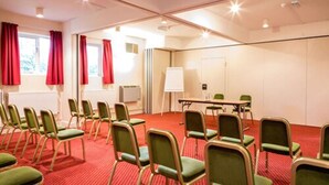 Ein Konferenzraum mit grünen Stühlen, einer Whiteboard-Tafel und einem roten Teppich.