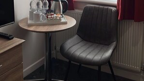 Ein Hotelzimmer mit einem runden Tisch, einem Sessel, einem Fernseher und einem Fenster mit roten Vorhängen.