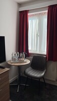 Habitación de hotel con una mesa redonda, una silla, un televisor y una ventana con cortinas rojas.