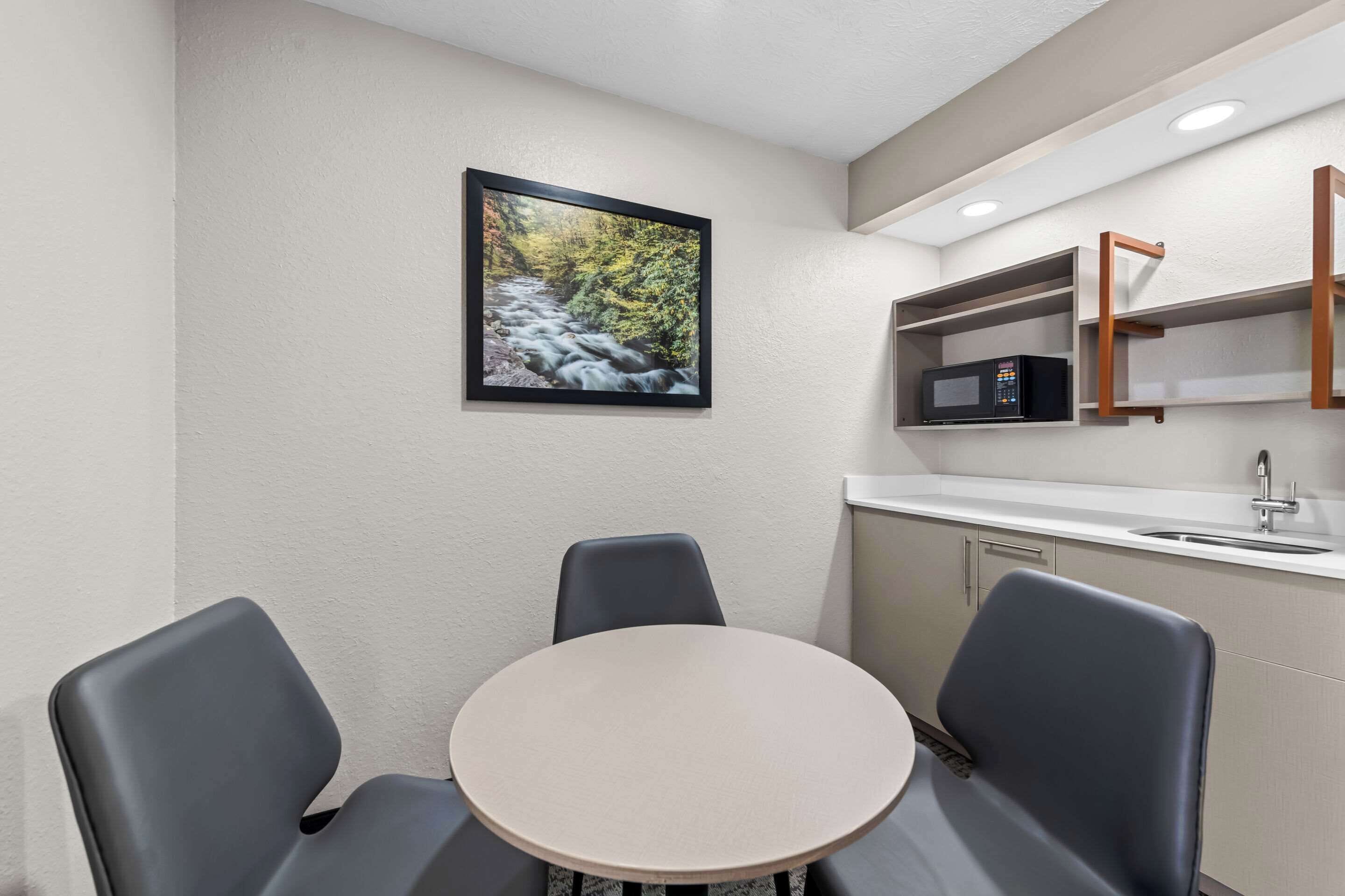 A small, modern kitchen with a round table and two chairs, a microwave, and a sink.