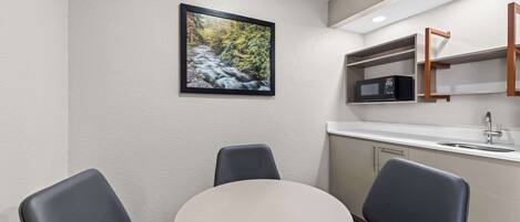 A small, modern kitchen with a round table and two chairs, a microwave, and a sink.