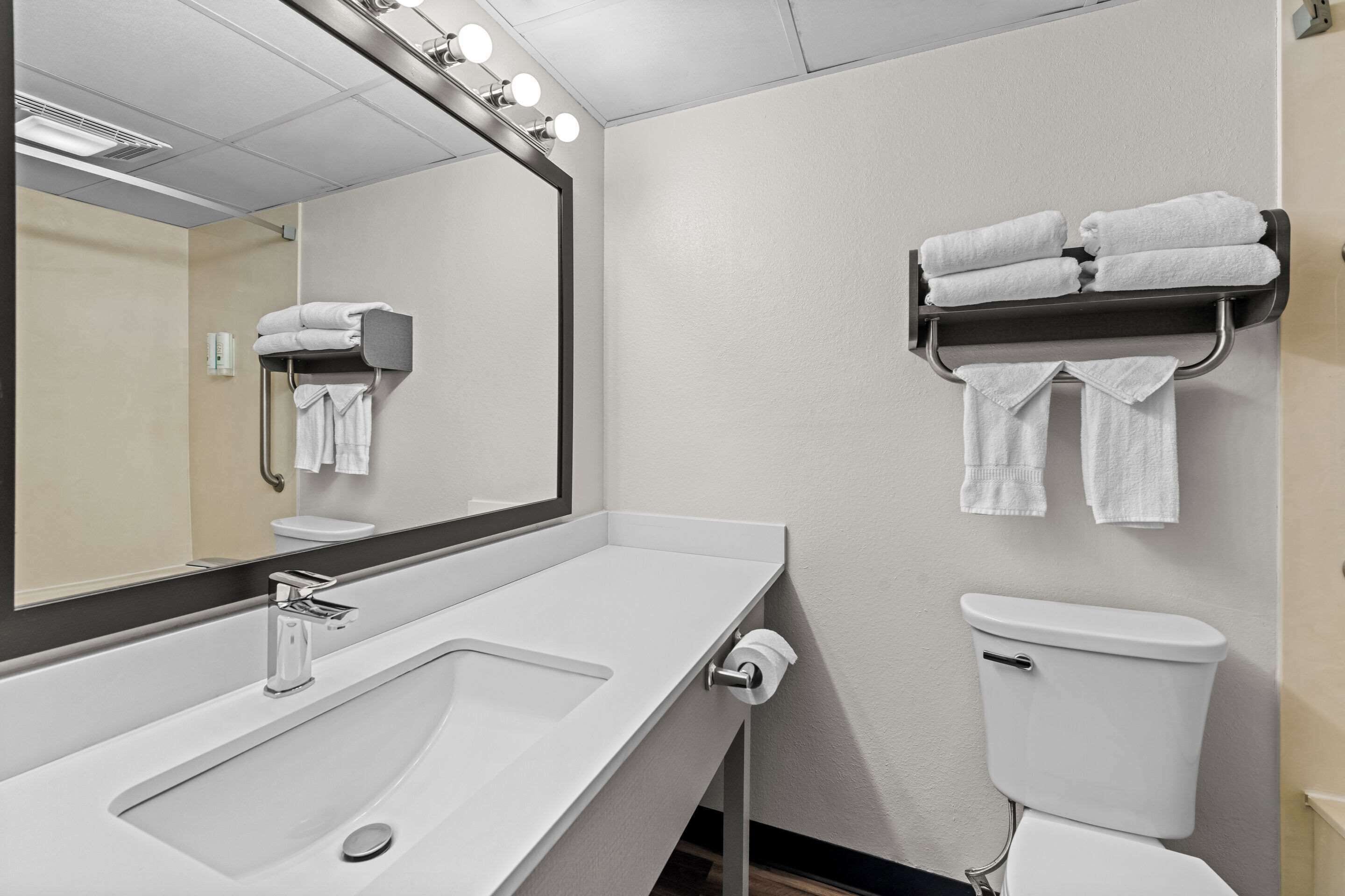 Un baño moderno con un lavabo blanco, un espejo con luces, un inodoro y un perchero con toallas dobladas.