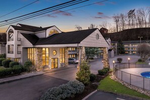 Stunning hotel entrance with a covered walkway, flanked by two wings and surrounded by manicured lawns and a small pool.