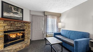 Una sala de estar con chimenea de piedra, un sofá azul, una mesa de centro y una cortina estampada.