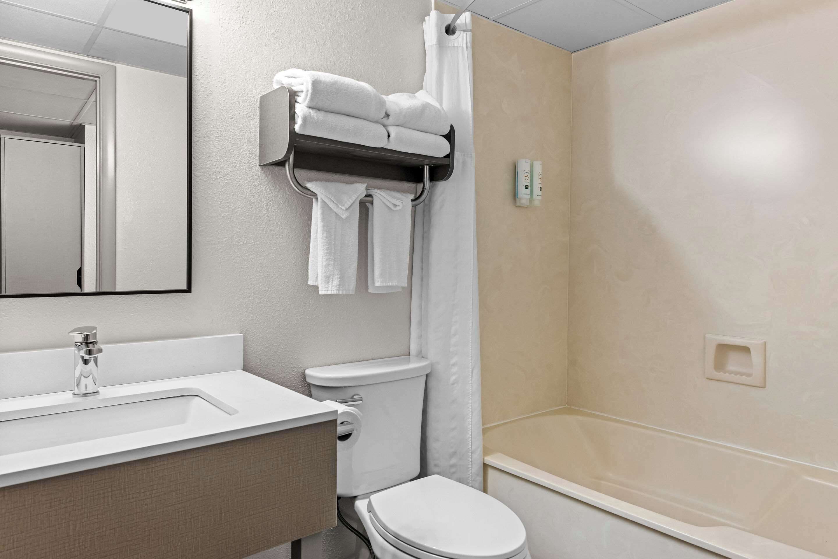 Un baño con lavamanos blanco, inodoro, toallero con toallas dobladas y cortina de ducha.