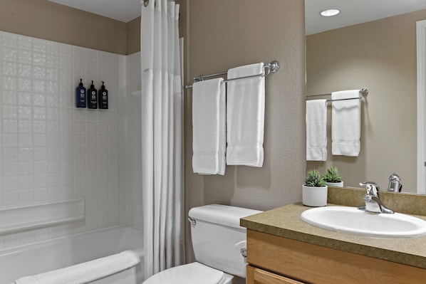 A bathroom with a white toilet, a sink with a mirror, and a shower area.