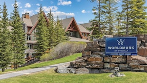 A sign for the Canmore-Banff Resort's Worldmark by Wyndham, featuring a stone wall and a wooden staircase leading to a lodge with a sloped roof. - WorldMark Canmore - Banff (Canmore)