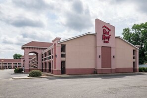 Un hotel Red Roof Inn con una entrada central, una zona de estacionamiento techada y cielo despejado.