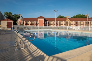 Una piscina con barandilla metálica, rodeada por una cerca blanca, con un edificio al fondo.