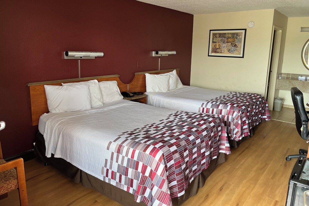 A hotel room with two beds, a wooden headboard, a small desk, and a chair.