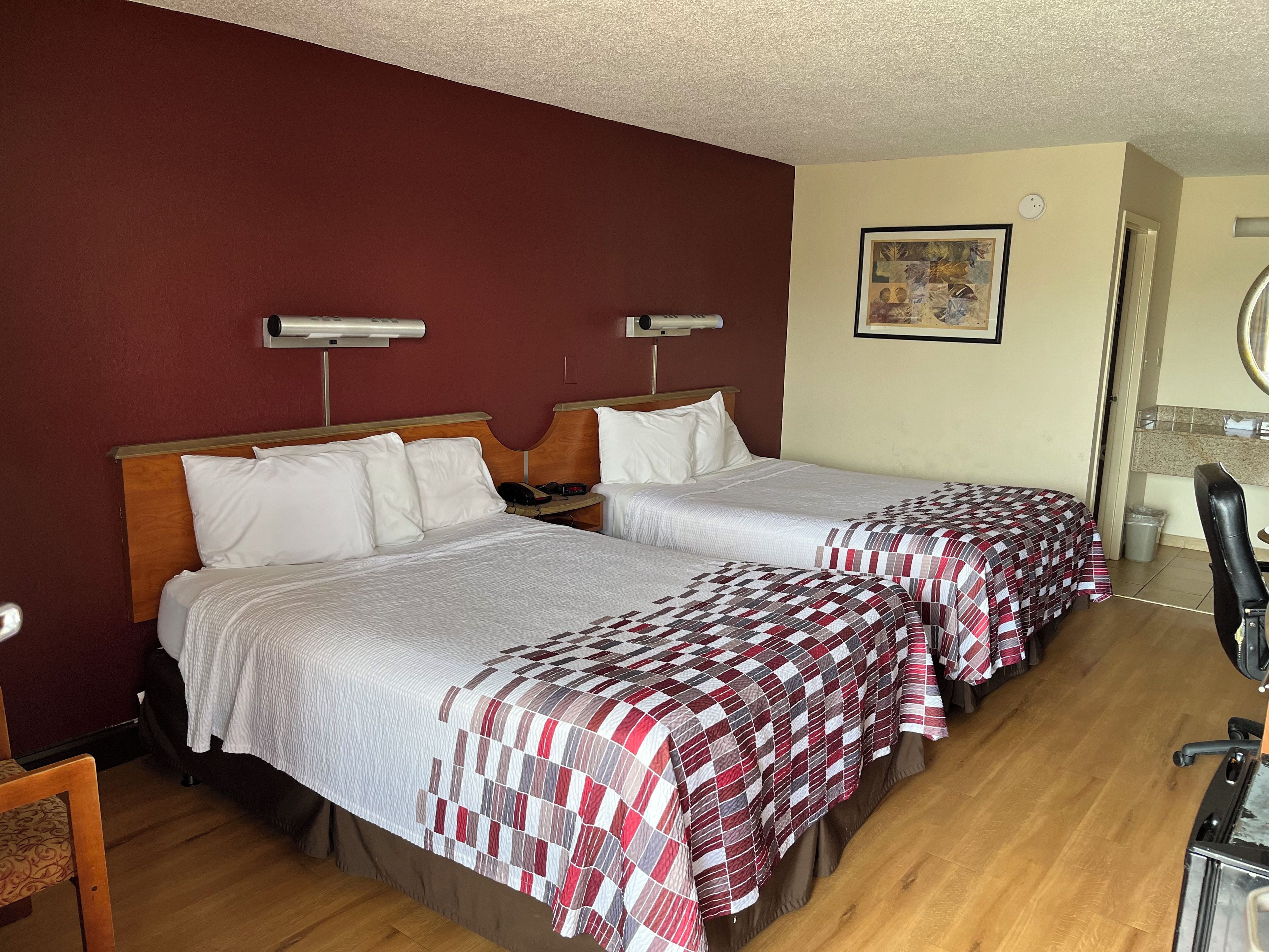 Een hotelkamer met twee bedden, een houten hoofdeinde, een klein bureau en een stoel.