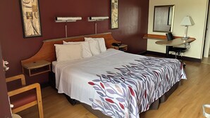 A hotel room with a large bed, wooden headboard, bedside tables, a desk, and a chair. - Red Roof Inn Virginia Beach - Norfolk Airport (Virginia Beach)